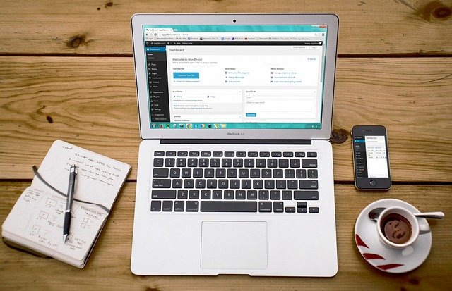 Un laptop deschis pe panoul WordPress lângă o agendă și o cafea, ilustrând importanța unui web design bine structurat. how to create a website