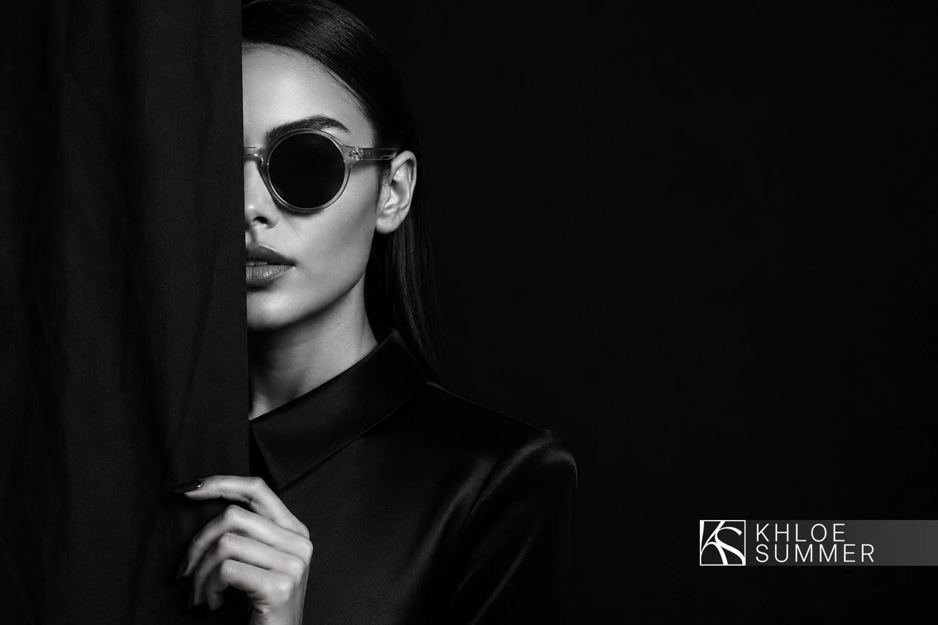 Portret artistic alb-negru cu un model feminin purtând ochelari de soare rotunzi și haine negre de lux, cu logo-ul Khloe Summer în colț, realizat de FloBold.