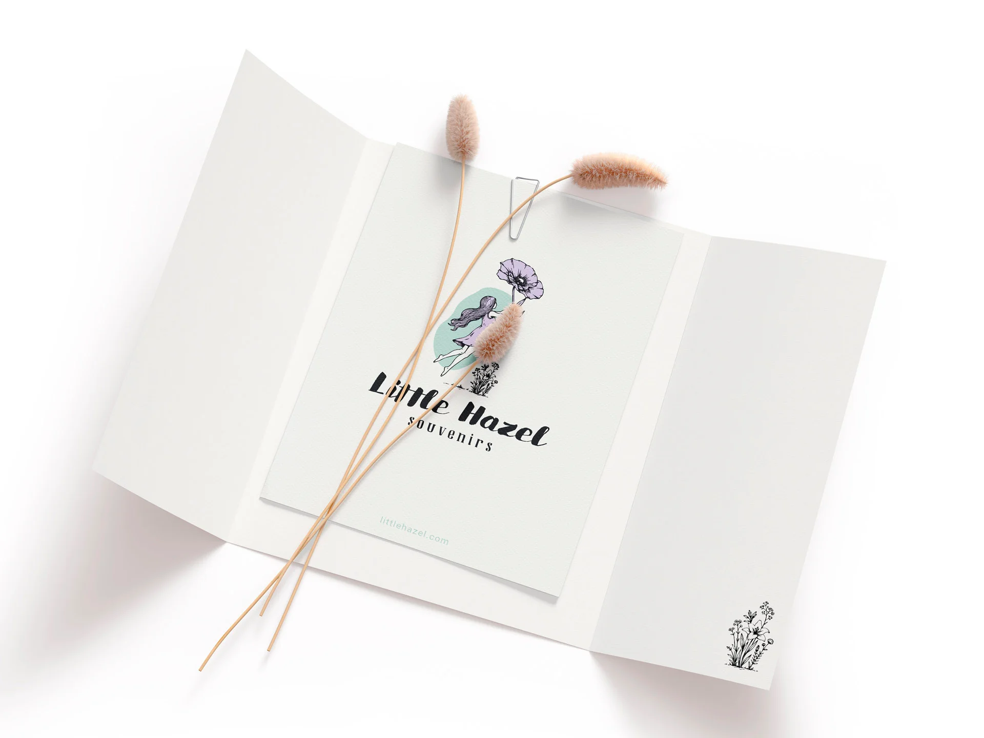 Mockup cu o mapă de prezentare albă deschisă în trei panouri, personalizată cu logo-ul Little Hazel și un element floral mic, decorată cu plante uscate, realizat de FloBold.