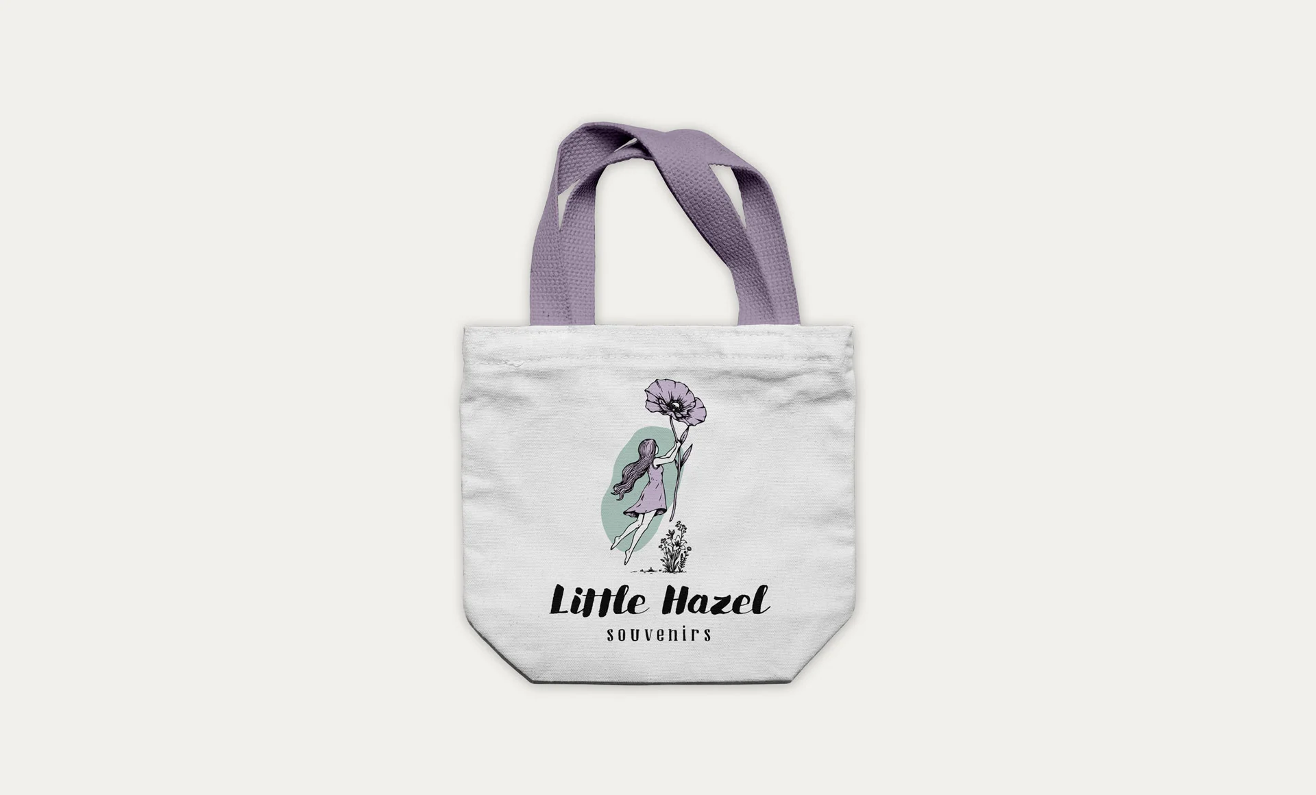 Sacoșă din bumbac organic de culoare albă, cu mânere mov și logo-ul ilustrat Little Hazel Souvenirs imprimat pe centru, realizată de FloBold.